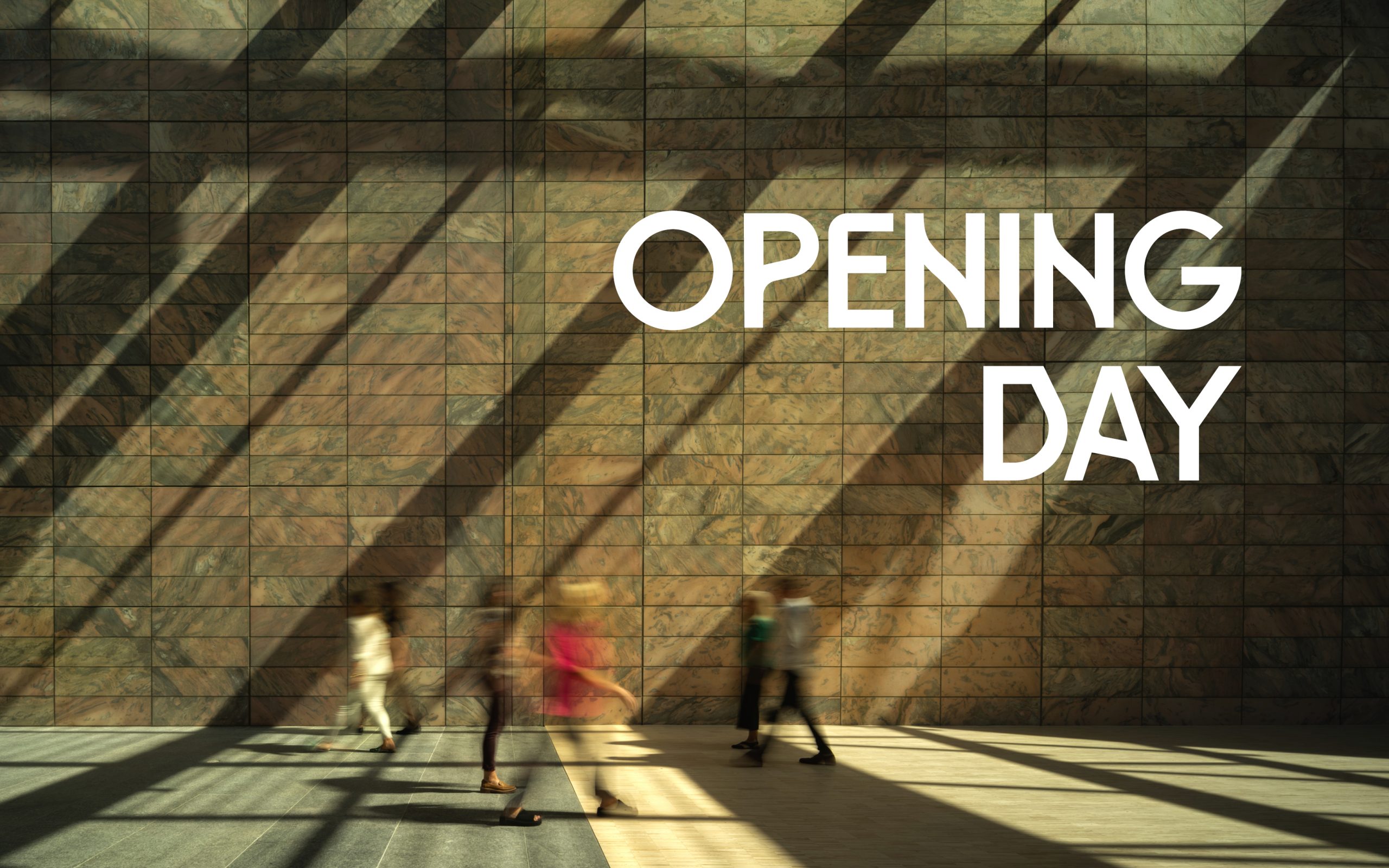 A large wall with geometric shadows and the words "OPENING DAY" in bold white letters. Several people walk by, casting blurred silhouettes on the ground and wall in the sunlight.