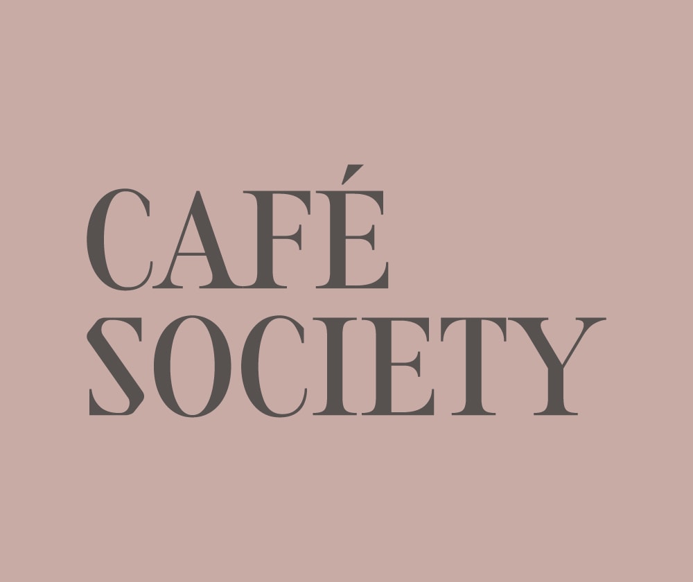 The image displays the words “CAFÉ SOCIETY” in bold, uppercase, serif font against a light pink background.