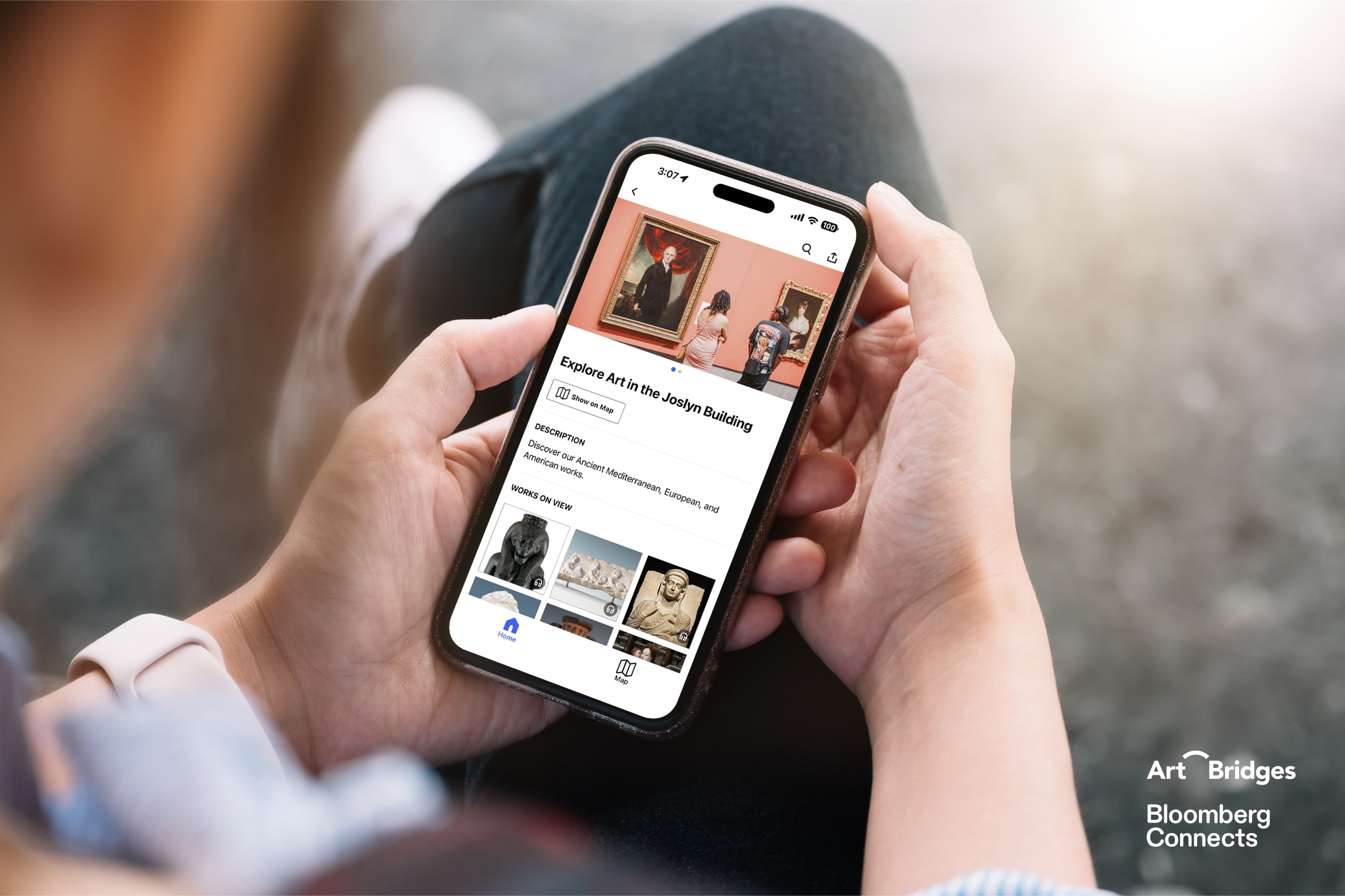 Person holding a smartphone displaying an art app with photos of artworks and museum galleries. Art Bridges and Bloomberg Connects logos are visible in the lower right corner.