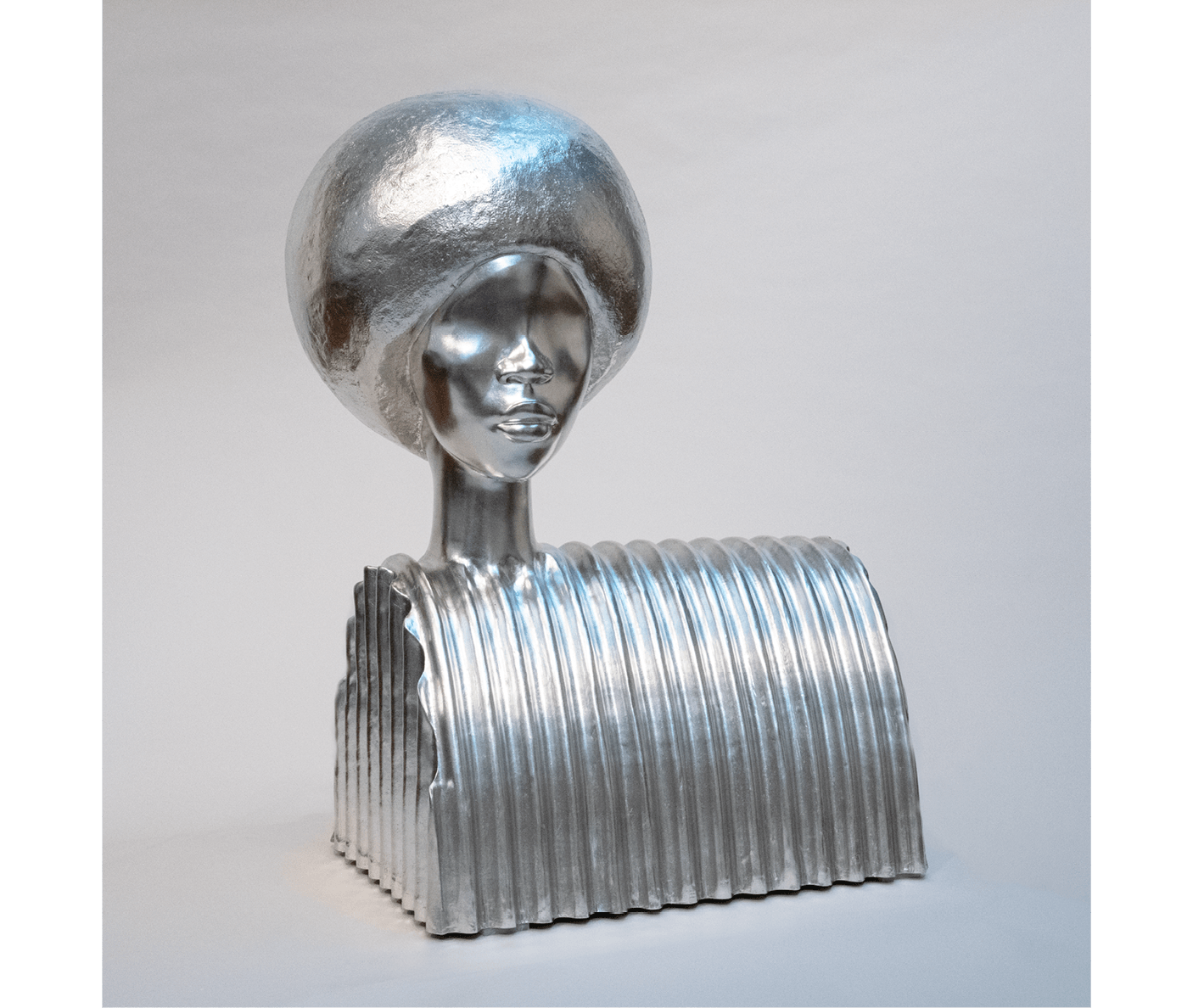 Sculpture of a woman's head and shoulders in metallic silver. The hair is styled in a large, spherical afro, and the shoulders are abstractly represented with vertical ridges on a boxy base. The overall texture is smooth and reflective.